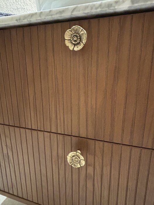 Kommod med vertikala trälinjer och mässingsblommiga knoppar från Dims, placerad under en marmorskiva.