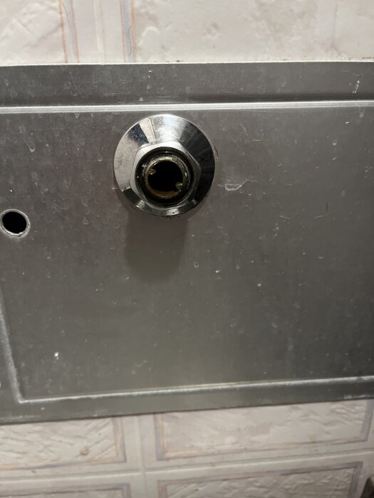 Metallplåt med montering för röranslutning, delvis demonterad, synlig gänga i röranslutningen.