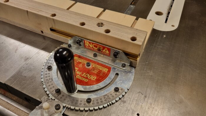 Snickarsläde med hål och t-track på en såg, märkt med "INCRA" och graderad vinkelanvisning.