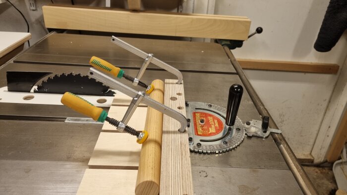 Sågmaskin med specialanpassad släde för att hålla runda träbitar stabila, försedd med skruvtvingar och dubbla infästningar för vinkelsågning.