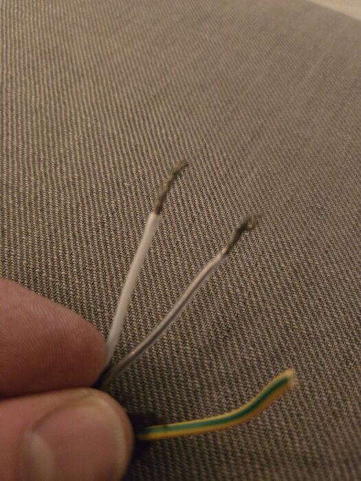 Närbild av tre elkablar; en vit, en genomskinlig och en gulgrön, fasthållna av en hand.