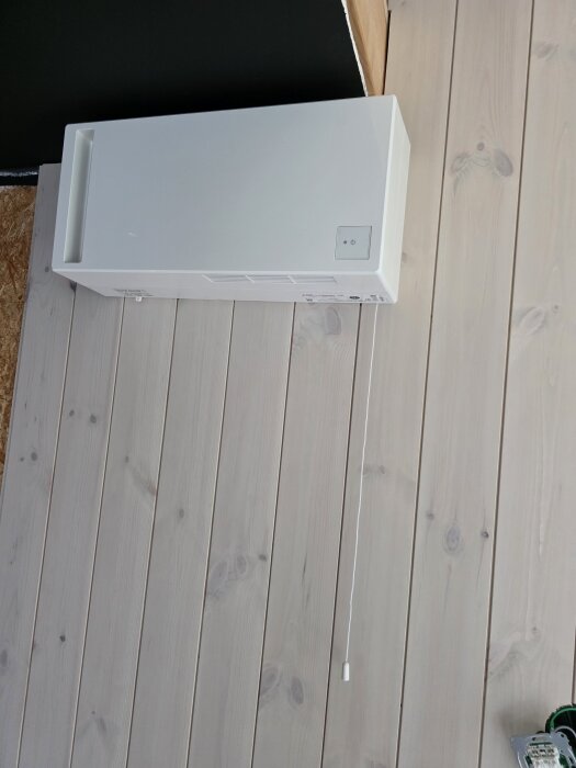Vit mini FTX-ventilationsenhet monterad på en innervägg med träpanel utan lister, skapar shadow gap.