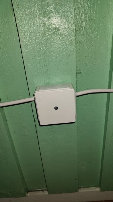 Vit strömbrytare monterad på grön panelvägg.