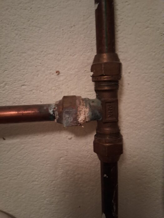 Kopparrör och korroderad koppling med T-koppling i källarmiljö, diskussion om avstängning och pluggning av vattenledning.