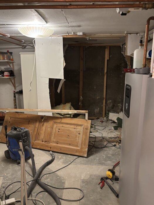 Rivning av badrum, trasig vägg och dörr på golvet, dammsugare och verktyg synliga.