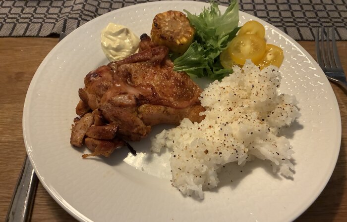 Tallrik med grillad kyckling, ris med krydda, sallad, majonnäs, grillad majs och gula tomater.