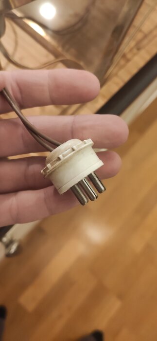 Närbild på en rund lamphållare med fyra pinnar, hållen i en hand, mot en suddig bakgrund.