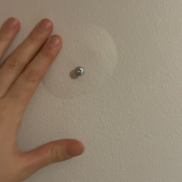 En hand bredvid en bubbla på en betongvägg från 50-talet, med en skruv nära bubblan.