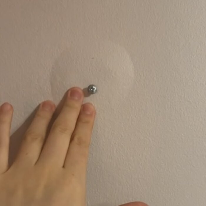 Hand vid skruv och bubbla i en beige vägg.
