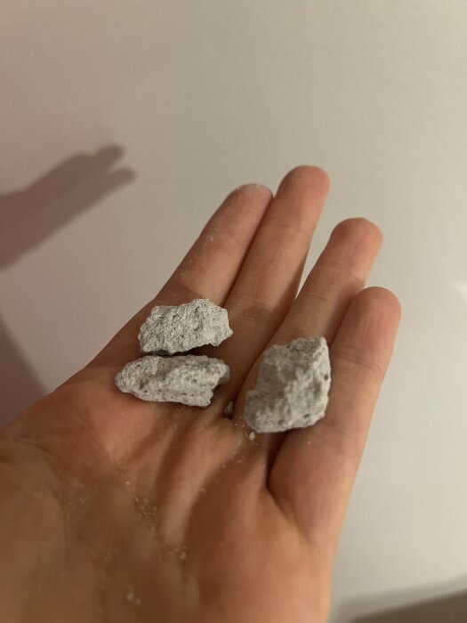 Hand håller tre små bitar av sprucken betong efter borrning.
