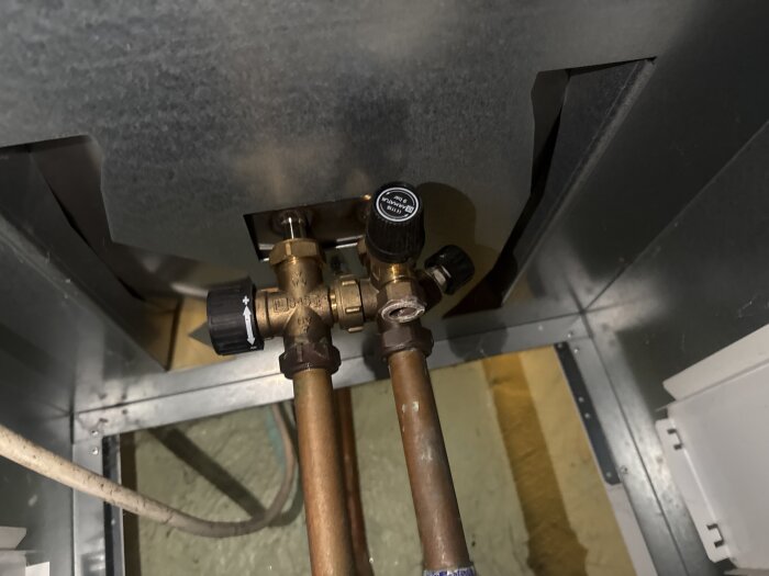 Ventiler och rör i ett värmesystem under en metallpanel, diskussion om problem med elementens värme i ett hus.