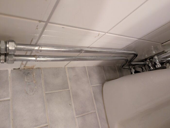 Buckliga kopparrör i badrum bredvid kaklade väggar och golv.