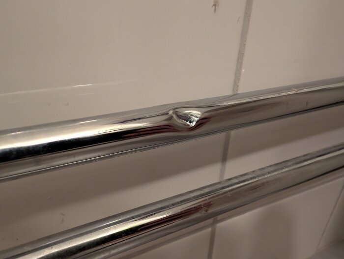 Kopparrör i badrum med en synlig buckla mot en kakelvägg.