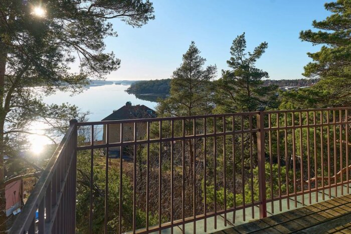 Balkongutsikt över sjö med träd och ett hus i bakgrunden, del av vacker 30-tals villa som behöver renoveras.