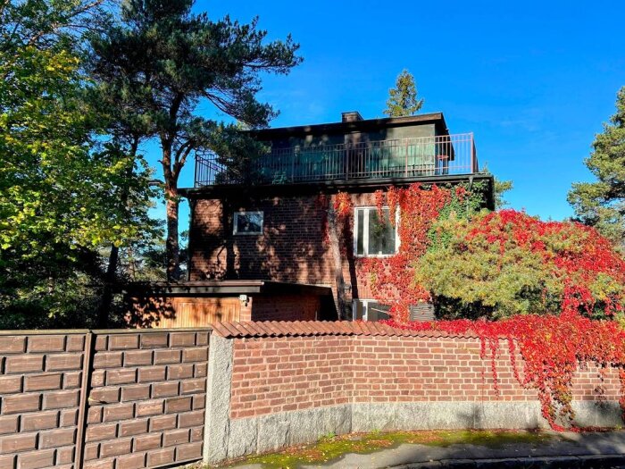 Vacker tegelvilla från 30-talet med röd klätterväxt på fasaden och omgiven av träd; behöver renoveras.