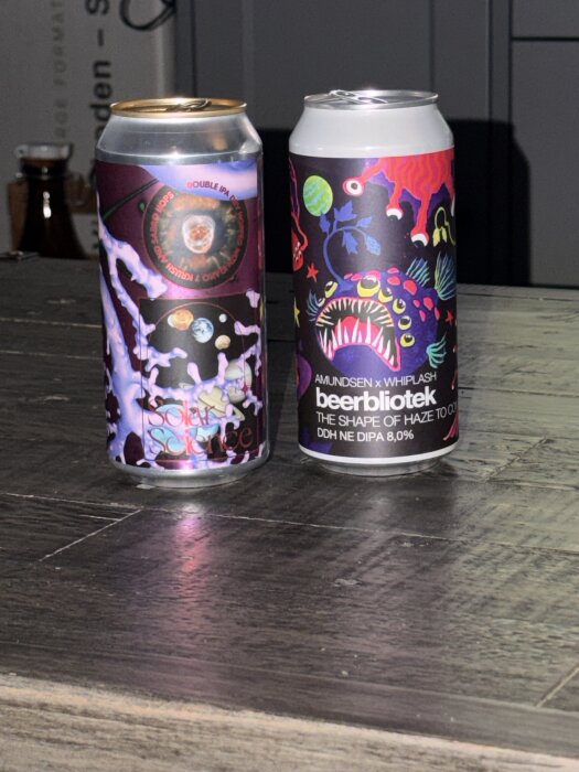 Två burkar med öl på ett bord, märkena är Elmeleven Solar Science och Beerbliotek The Shape of Haze to Come, båda med färgglada etiketter.