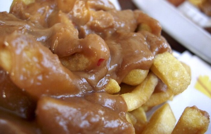 Pommes frites toppade med satsås, närbild.