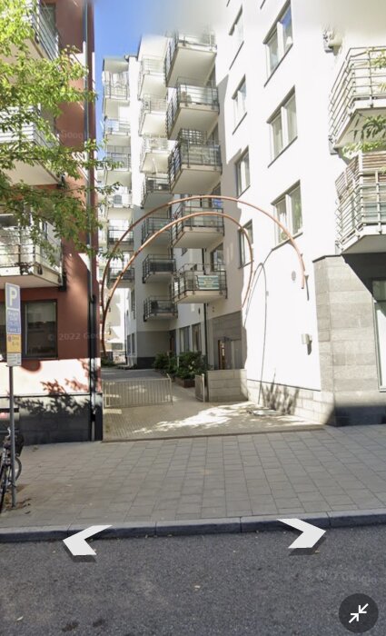 Modernistisk byggnad med balkonger, del av stadsplanering med öppet kvarter, solbelyst fasad och port.