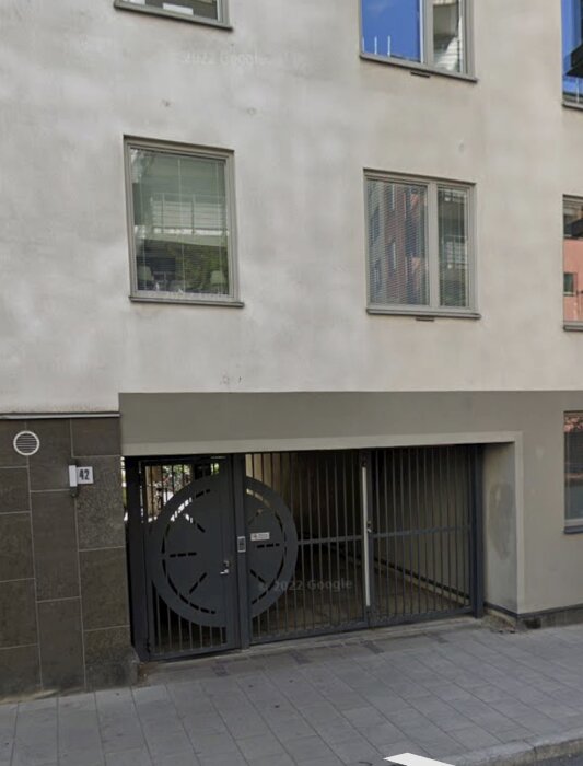 Fasad av en modern byggnad med fönster och en garageport försedd med ett runt dekorativt mönster, belägen vid en trottoar.