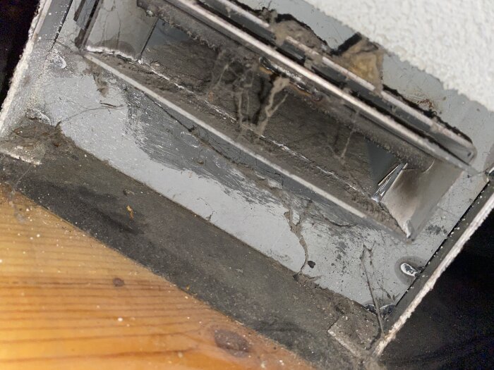 Ventil på baksidan av en spis, belägen nära golvet, med en justerbar lucka för luftflödet.