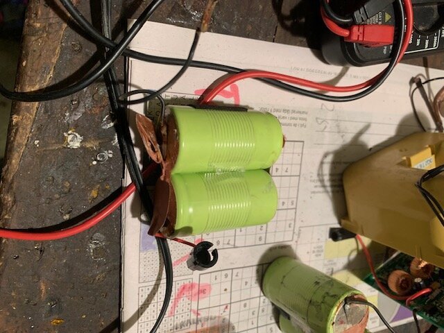 Gröna C-batterier urtagna från ett Topcon-laserbatteripaket, kopplade med kablar på en arbetsbänk.