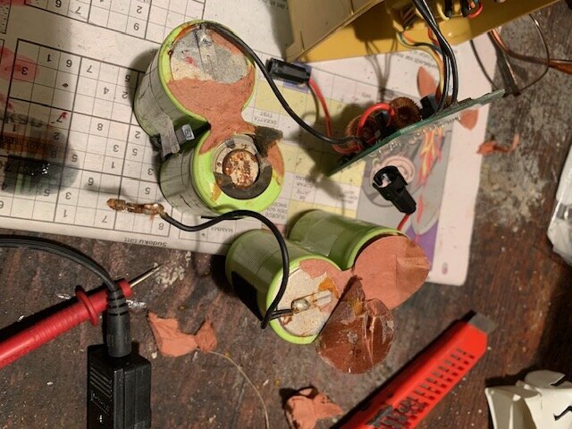 Gröna C-batterier isärtagna och sammankopplade, ligger på en arbetsyta med elektronikdelar och verktyg runtom.