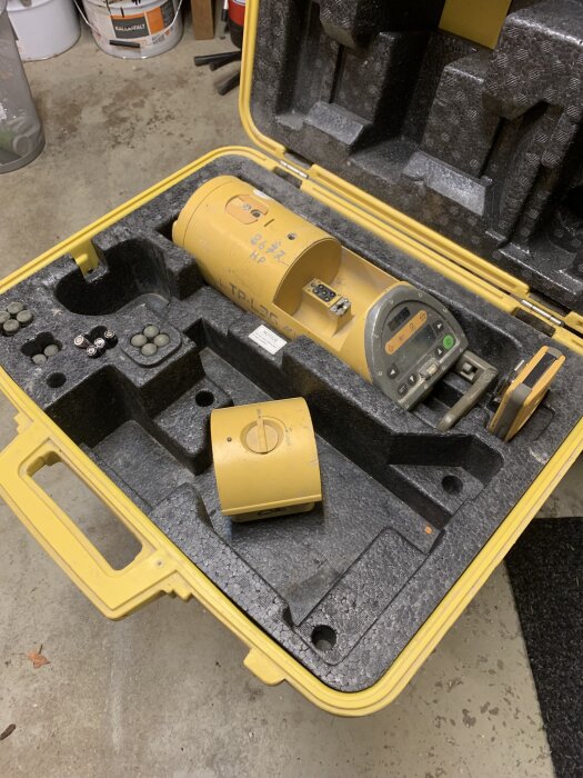 Gul Topcon laserenhet med tillbehör i en öppen plastväska.