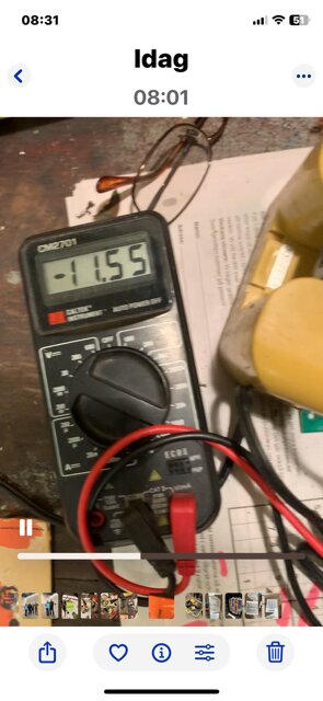 Multimeter visar spänningen 11,55 volt bredvid ett Topcon Laser-batteripaket och några lösa komponenter på ett bord.