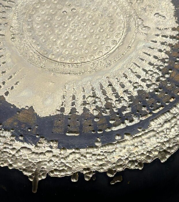 Närbild av en aluminiumkastrulls botten med synliga tecken på förslitning och slitage.