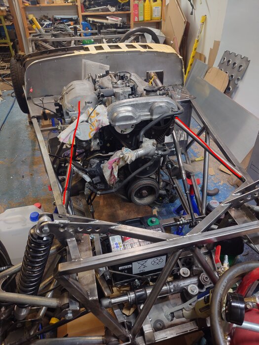 V-motor i en Super Seven med fokus på ramkonstruktion och borttagna rör, omgiven av verktyg och delar i garage.