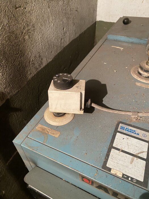 Gammal värmepanna med termostat, placerad i källare, delvis rostig och dammig, med reglage på ovansidan.