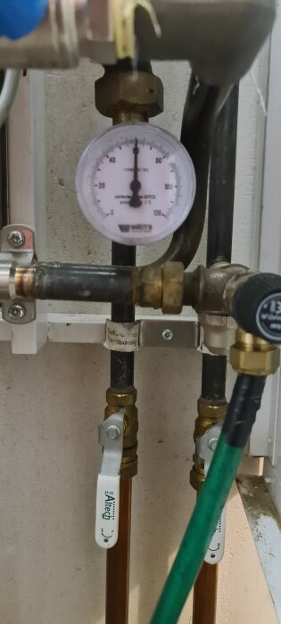 Termometer på värmesystem, visar temperatur vid radiator framledning, grader från -20 till 120. Rör och ventiler synliga i bakgrunden.