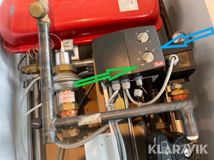 Ventil och styrmodul för värmesystem med pilar som pekar på rattar och mätare, kopplade till rör och komponenter i systemet.
