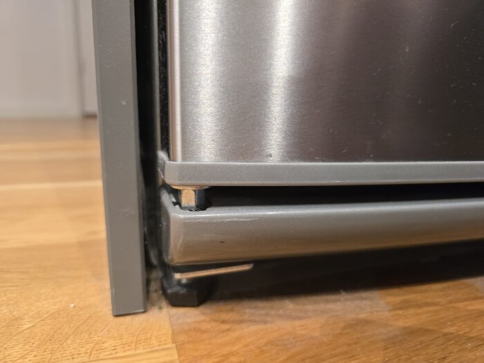Närbild på ett kylskåpsgångjärn där en mutter är synlig. Dörren verkar inte stänga som den ska på grund av gångjärnsproblemet.