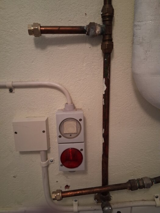 Vattenrör och en röd lampa i en tvättstuga, inga synliga läckor, kopplingar ser nyligen installerade ut.