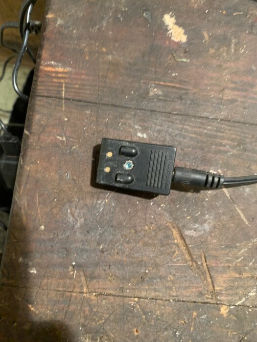 Svart batteriladdkontakt på en träarbetsbänk, delvis ansluten med kabel.