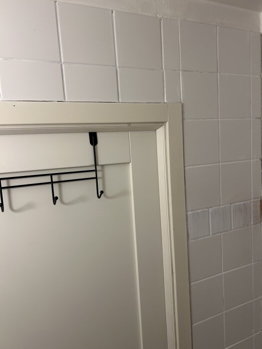 Vitt kakel i ett duschrum med ljust fogmellanrum vid en dörr, en kakelrad har svagt synliga terracottafärgade kanter.