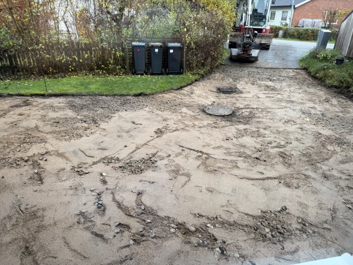 Uppgrävd mark med borttagen asfalt och justerade höjder, grävmaskin i bakgrunden.