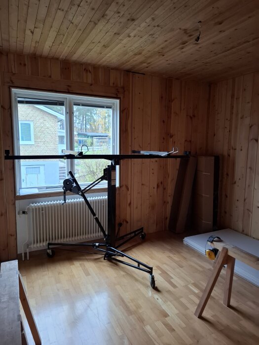 Trärum med trägolv, gipsskivor lutade mot väggen, ett fönster och verktyg på golvet. Ett element under fönstret.