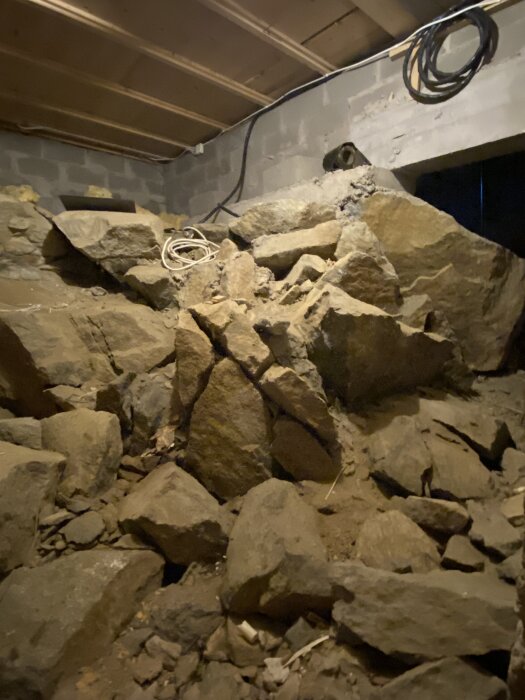 Stenar och kablar i ett bergrum under konstruktion med exponerade takbjälkar och betongväggar.