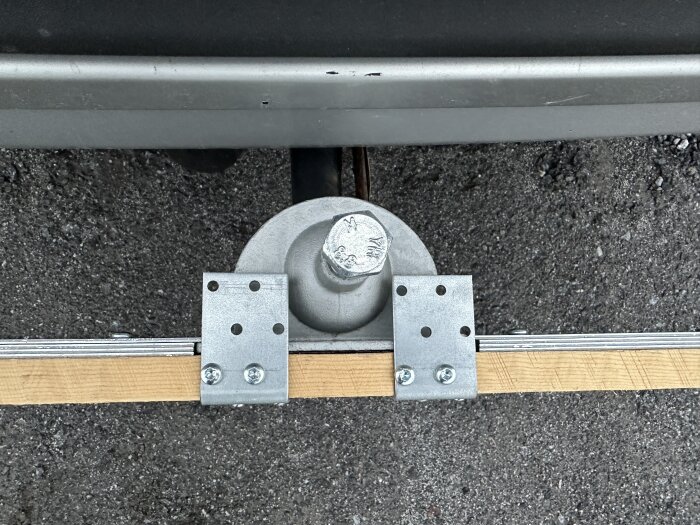 Hålplattor och vinkeljärn på träbit monterad på en metallstång, för nivåjustering och fixering.