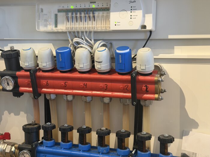 Golvvärmefördelare med sex ventiler monterade på röd och blå ledningar, en ventil läcker och märkena Uponor och Swegon syns på ställdonen.