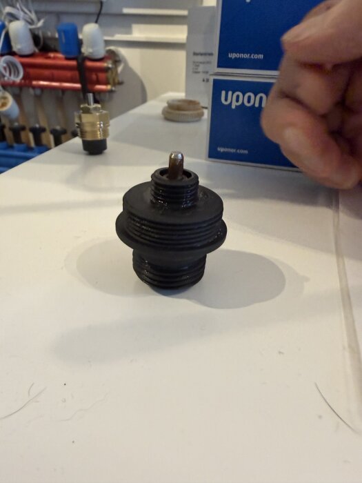 Fördelarventil till golvvärme med en läckande del på ett bord bredvid Uponor-förpackningar.