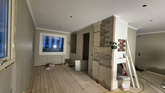 Renoveringsprojekt med nymålade väggar och synligt foder. Byggmaterial och element ligger på golvet, med ett ofärdigt hörn synligt.