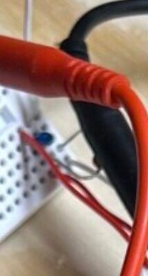 Röda och svarta kablar kopplade till ett experimentbräde med dolda komponenter i bakgrunden.