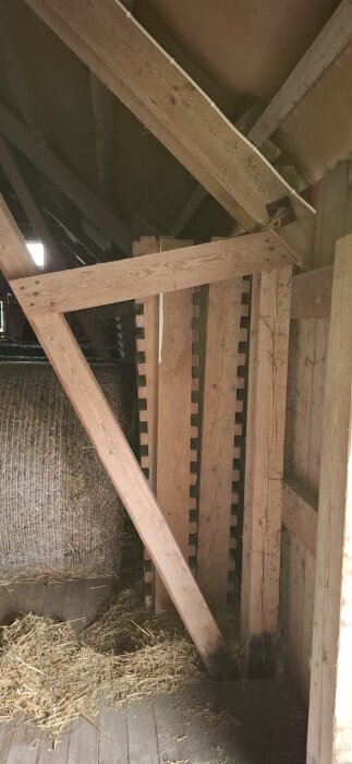 Takstol i en lada med träbalkar och stödstolpar. Hö och andra material syns på golvet intill.