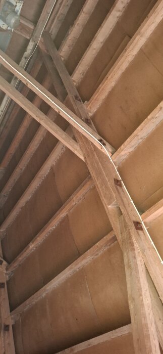 Takstol av trä i en lada, sedd snett underifrån. Vinklar och dimensioner synliga för hållfasthetsberäkning. Kabel längs bjälke.