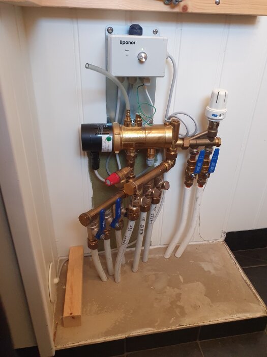 Golvvärmesystem med Uponor-kontroll, rör och ventiler synliga i tvättstugan på markplan. Inga tryckmätare är synliga på bilden.
