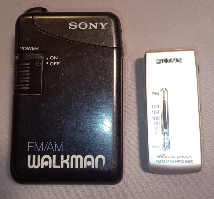 Två Sony fickradior, en svart Walkman FM/AM och en vit Walkman FM Stereo Mega Bass, båda från åttiotalet.