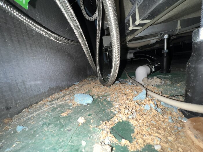 Insidan av badkarets inkakling med rör och kablar, smuts och skräp på golvet. Foto taget genom inspektionslucka.